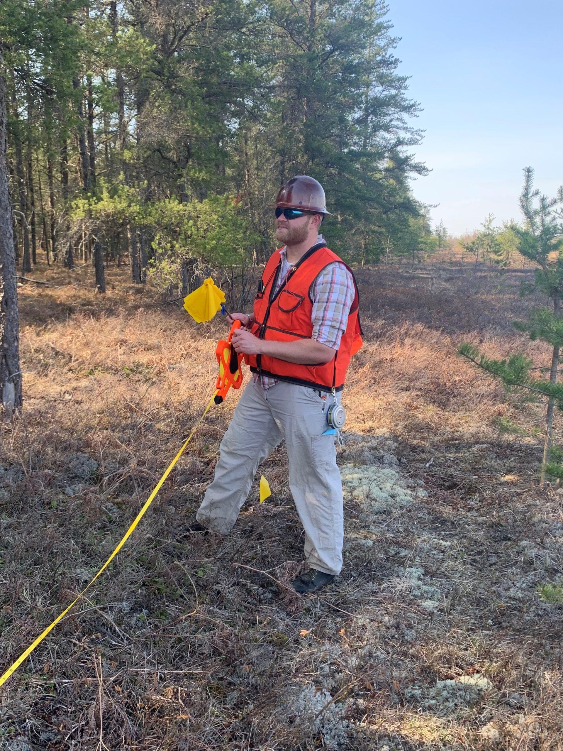 Hudson Cermak standing in a vest in the middle of a field at the edge of a forest